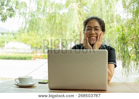 Asian Woman Student Working On Laptop With Earphone Looking At Camera.