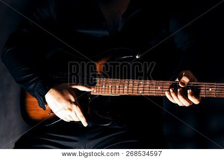 Six-string Electric Guitar In The Hands Of A Musician. The Fingers Of The Musician Touch The Strings