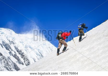 Two Mountain Trekkers On Steep Snowed Hill With Peaks Background