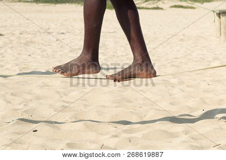 Closeup Man Feet Walking On Tightrope Or Slackline On Sandy Background. Slacklining Is A Practice In