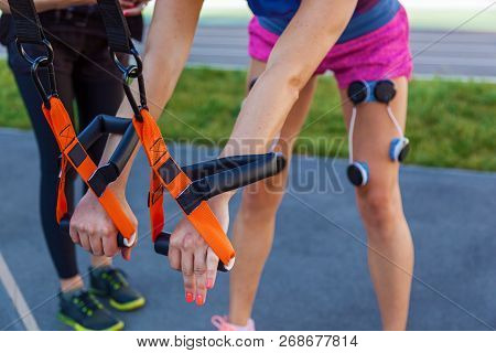The Girl Is Engaged In Fitness With An Electrostimulator. Exercises And Load On The Leg Muscles With