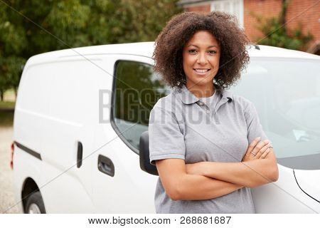 Young black female tradesperson standing next to her white van with arms crossed, close up