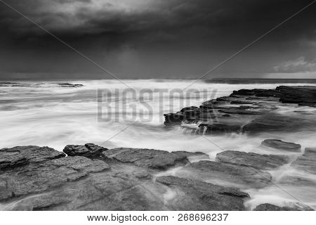 Waves Engulf The Rock Shelf As Moody Weather Increases Swells Along  Coastal Beaches As A Storm Move