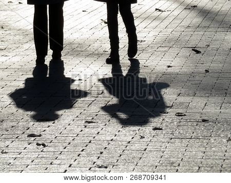 Silhouettes Of Two People Walking Down The Street. Two Women Outdoors, Shadows On Pavement, Pedestri