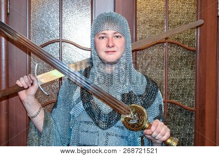 A Man Dressed Up In A Knights Hauberk At Home In His Room. Knights Sword In The Hands Of A Man. Knig