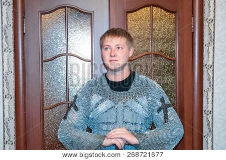 A Man Dressed Up In A Knights Hauberk At Home In His Room. Knights Sword In The Hands Of A Man. Knig