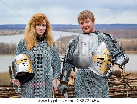 Knight With His Wife In Armor And Chain Mail. Knightly Armor And Weapon. Semi - Antique Photo.