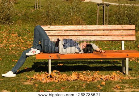 A Drunk Young Woman Sleeping On A Bench In The Day.a Young Woman Holding A Bottle Of Alcohol In Her 