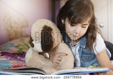 7 Years Old Girl Reading A Book On Bed