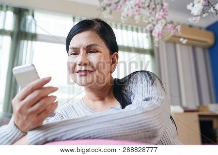 Smiling Senior Vietnamse Woman Reading Text Message In Her Smartphone
