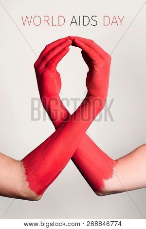closeup of the arms of two men painted red forming a red awareness ribbon and the text world aids day against an off-white background