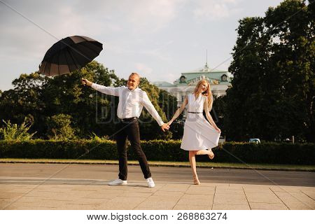 Young Couple Jump Up With Black Upbrella. Lovely Cuople Have Fun