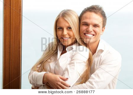 Unge lykkelige par hugging derhjemme med en smuk havudsigt bag deres vindue