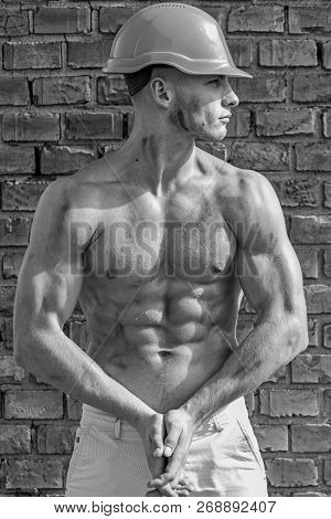Builder With Muscular Torso And Helmet, Brick Wall On Background. Sexy Builder Concept. Builder With