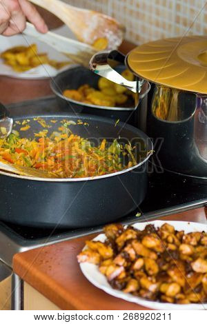 View Of The Kitchen. Pots With Cooked Food On The Stove.the Man Cooks Chicken Meat, Fried Potatoes A