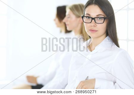 Attractive Businesswoman At Meeting Or Conference Against The Background Of Colleagues. Group Of Bus