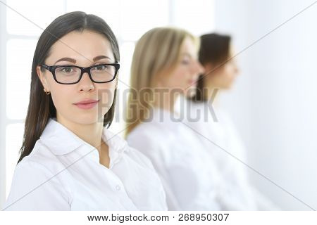 Attractive Businesswoman At Meeting Or Conference Against The Background Of Colleagues. Group Of Bus