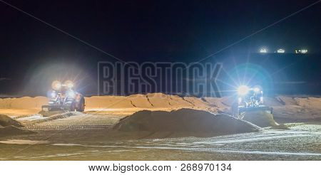 Two Ground Workers Working At Night In Bulldozers At The Beach Moving The Sand