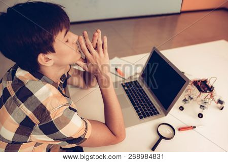 Upset Teenager In Shirt Programming Robot At Home. Young Man In Shirt. Using Laptop. Modern Hobby Co