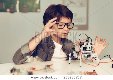 Boy Sitting At Desk And Constructing Robot At Home. Young Boy In Shirt. Indoor Joy. Modern Hobby Con