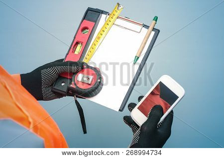 Building Contract. Fix List. Builder Is Holding Note Pad And Mobile Phone With Blank Screen In His H