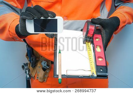 Building Contract. Fix List. Builder Is Holding Note Pad And Mobile Phone With Blank Screen In His H