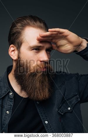 Young Hipster Man With Long Perfect Beard Looking Far Away On Gray Background