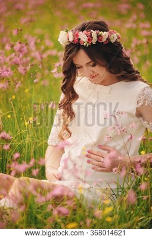 Portrait Of A Pregnant Woman Sitting In Fieid Of Pink Flowers. Young Beautiful Pregnant Girl With A 
