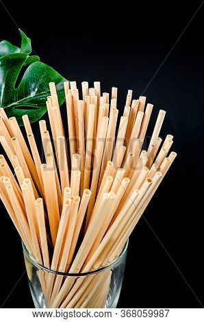 Wheat Straw For Drinking Water In Glass With Green Leaf On Black Background. Zero Waste Concept.