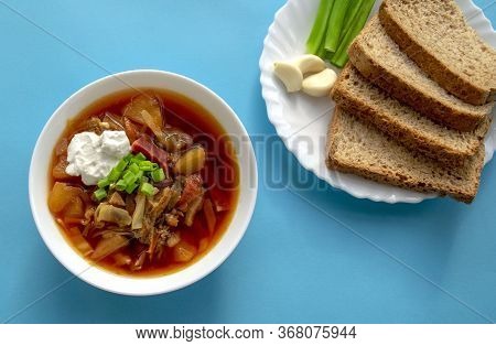 Borscht Soup In A White Bowl With Brown Bread, Green Onion And Garlic On Blue Background. Famous Tra