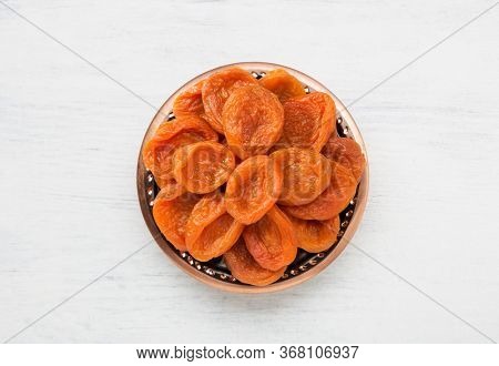 Bronze plate with dried apricots on the white wooden table.  Top view.
