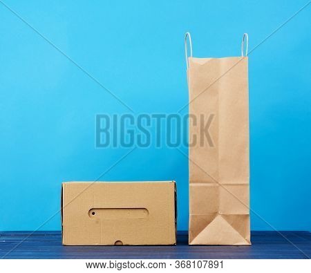Paperr Box And Brown Paper Bag With Handles Stands On A Wooden Background, Black Background, Copy Sp