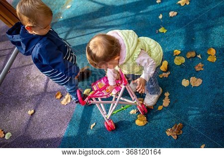 Little Cute Toddler Boy And A Beautiful Year-old Baby Girl In Blue Clothes Play In A Pink Toy Stroll