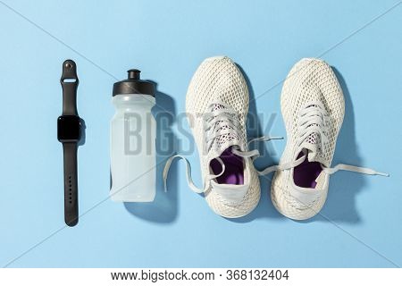 White Running Shoes, A Sports Watch And A Water Bottle On A Blue Background Under The Natural Light 