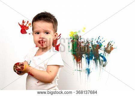 3 Year Old Boy Stained With Paint On The Background Of A Painted Wall. Colored Hands. The Concept Of