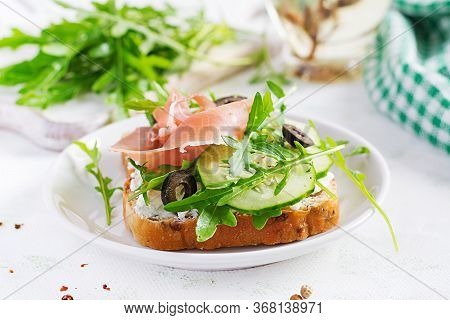 Sandwich With Prosciutto, Cucumber, Black Olives, Arugula And Feta Cheese On  Table.  Trend Food.