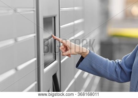 mail delivery and post service concept - close up of woman's hand choosing operation on outdoor automated parcel machine's touch screen