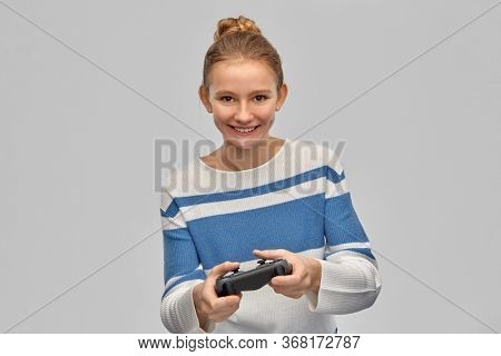 gaming, technology and people concept - happy smiling teenage girl in pullover with gamepad playing video game over grey background