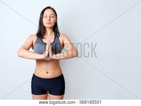 Portrait Of A Calm, Happy Woman On A Blue Background, Meditating With Her Hands Folded On Her Chest.