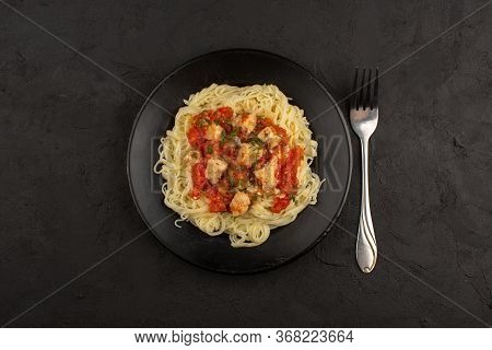 A Top View Pasta With Chiken Wings And Tomatoes Sauce Inside Black Plate On The Dark Floor