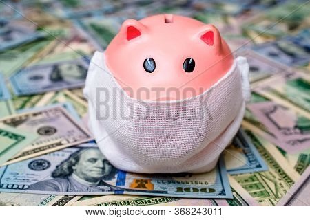 Piggy Bank In A Mask On A Background Of American Currency.the Concept Of Coronavrius Epidemic