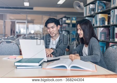 High School Or College Students Studying And Reading Together In Library. Student Use Laptop At Libr