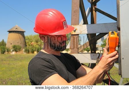 Tehnician In Red Helmet With Multimeter On The Electric Pole