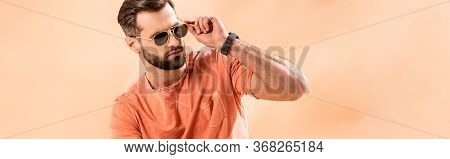Panoramic Shot Of Stylish Young Man Posing In Shorts, Summer T-shirt And Sunglasses On Beige