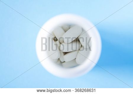 Pills Of Vitamin In The Opened White Plastic Container On Soft Blue Background.