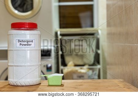 Fabric Powder Laundry Detergent With Scooper Against Washing Machine Background At Home