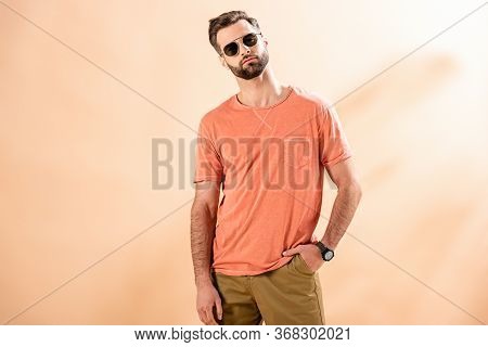 Fashionable Young Man Posing In Shorts, Summer T-shirt And Sunglasses On Beige