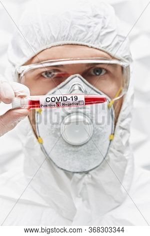 COVID-19. Doctor, microbiologist, scientist in a protective suit, shows test tube with blood sample of an infected person on a white background. Coronavirus test.