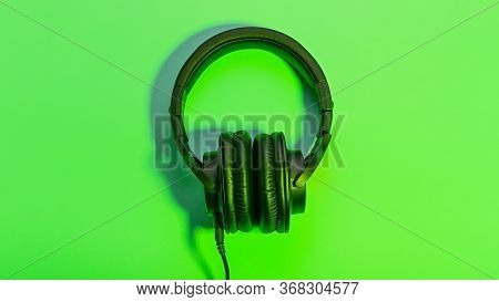 Black Overhead Headphones Neon Background, Copy Space. Modern Technology Flat Lay With Over-ear Earp