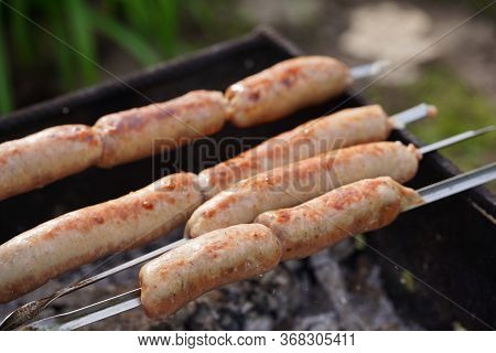 Close Up Of Toasted Sausages On Skewers. Succulent Kupaty Roasting On Chargrill. Concept Of Picnic O